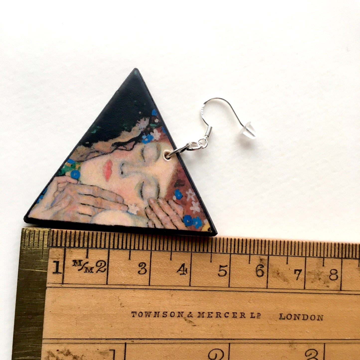 Klimt triangular earring nearby a rule that indicate the measurement of 4, 5 cm of his side.