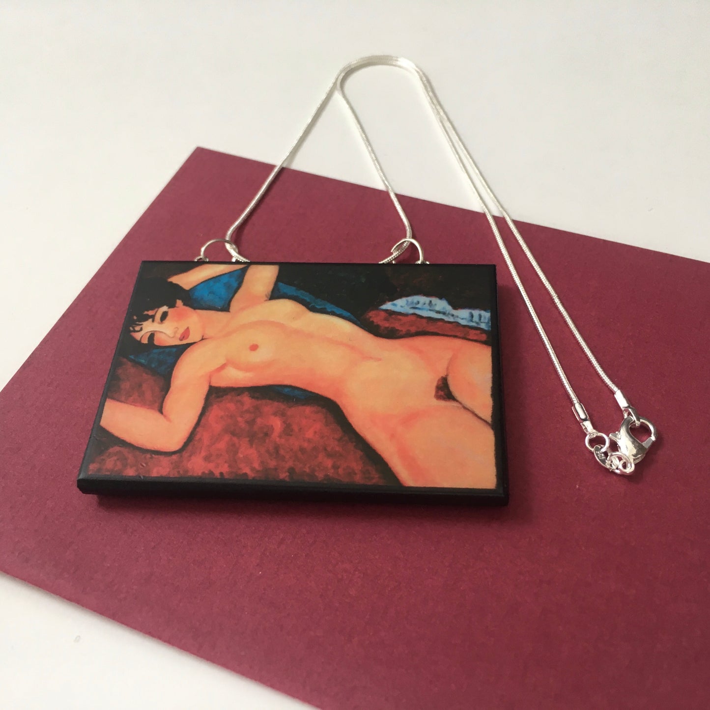 Amedeo Modigliani necklace handmade from sustainable wood by Obljewellery. The statement rectangular pendant with the painting of the nude female reclining on a red sofa on the blue cushion.
