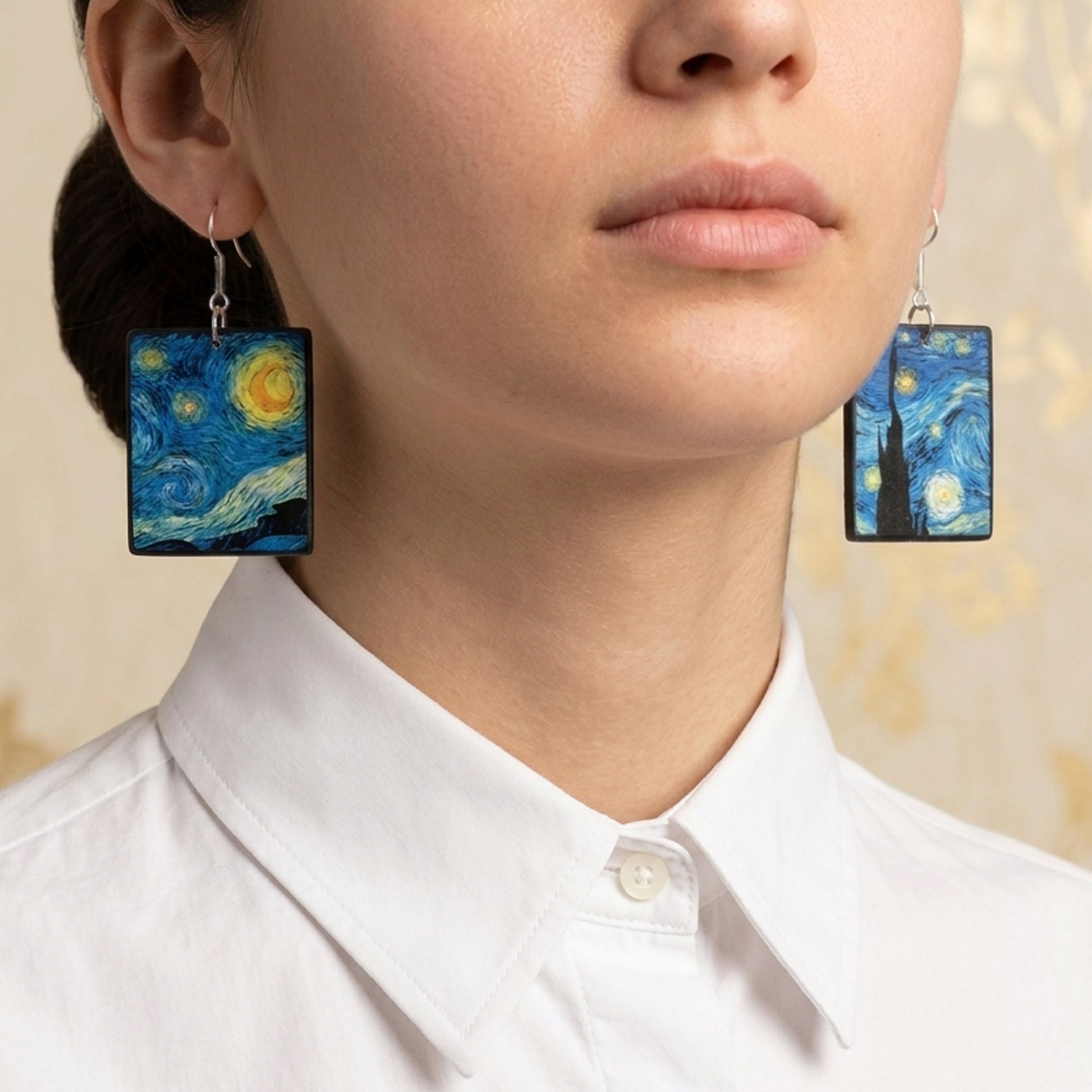 #A close-up of a model wearing rectangular drop earrings featuring Vincent van Gogh's 'The Starry Night' painting design, paired with a white collared shirt.