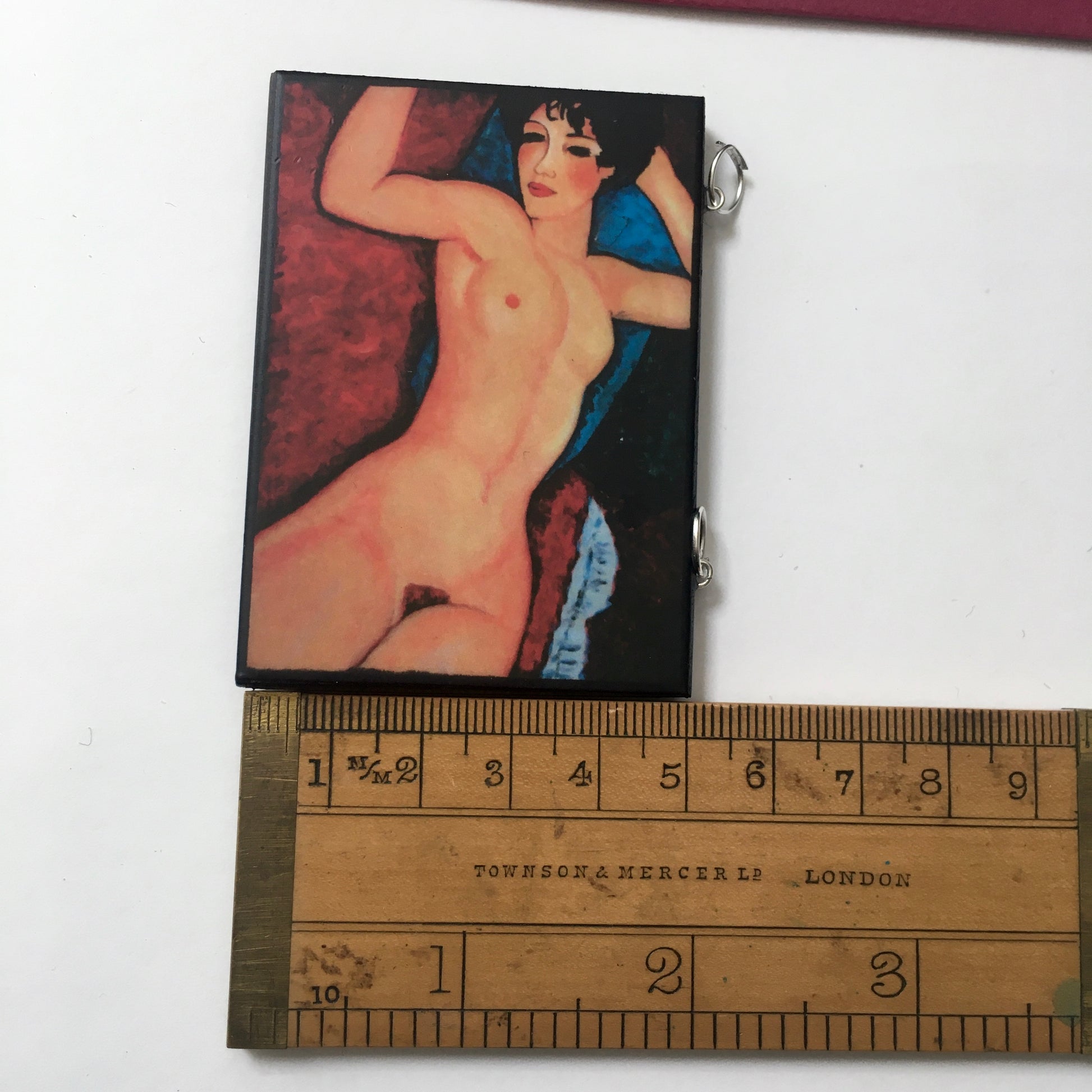 Pendant with an art detail of the sensual nude woman painting by Modigliani. The wooden, rectangular pendant near a rule shows the dimensions of 5 cm 