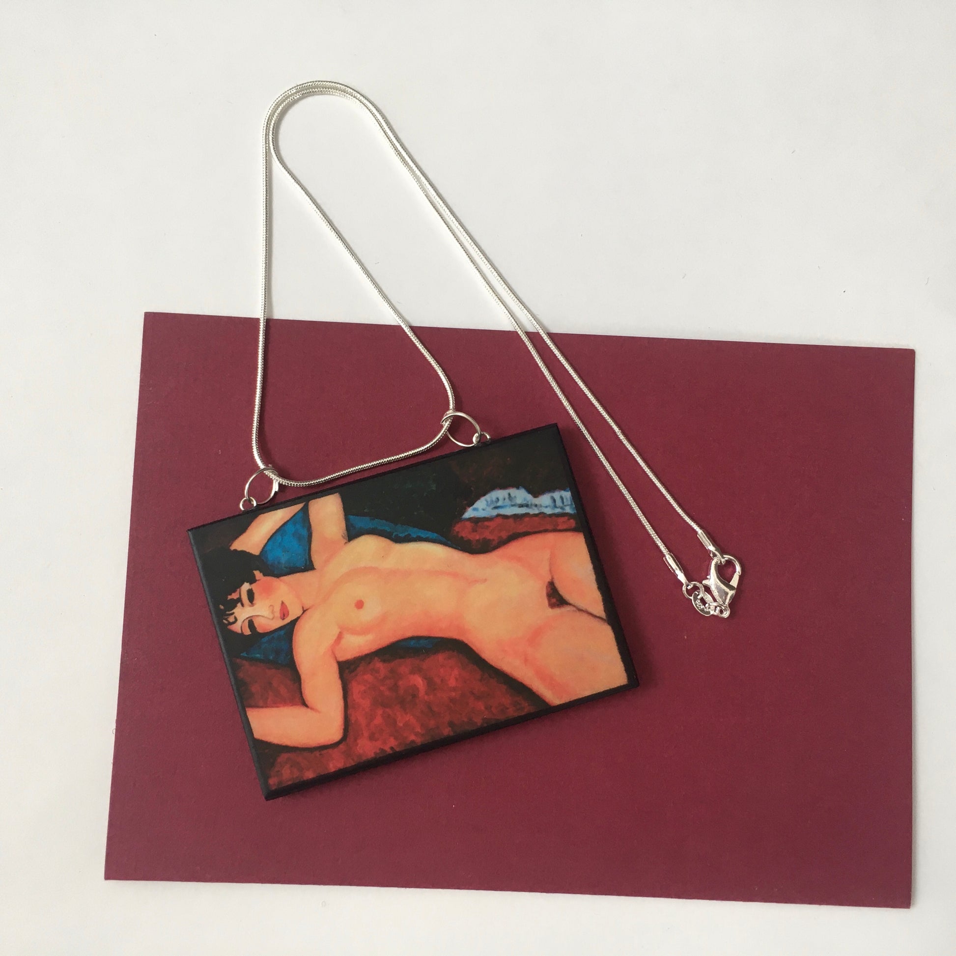 Amedeo Modigliani necklace handmade from sustainable wood by Obljewellery. The statement rectangular pendant with the painting of the nude female reclining on a red sofa on the blue cushion.