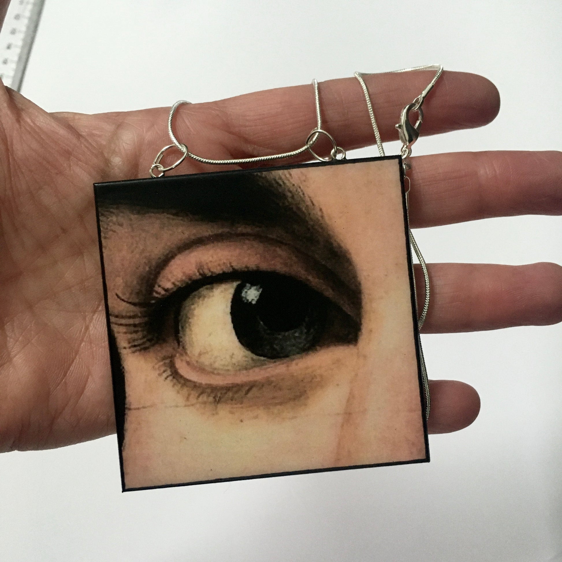 hand holding a Sustainable wood pendant with an eye detail taken from a Renaissance art painting by Antonello da Messina. Handmade by Obljewellery