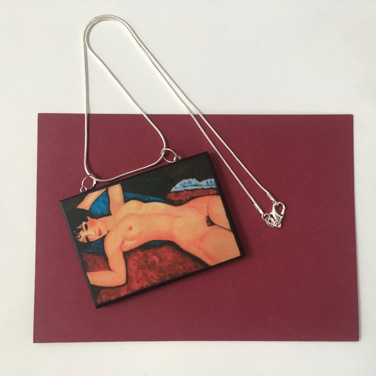 Amedeo Modigliani necklace handmade from sustainable wood by Obljewellery. The statement rectangular pendant with the painting of the nude female reclining on a red sofa on the blue cushion.